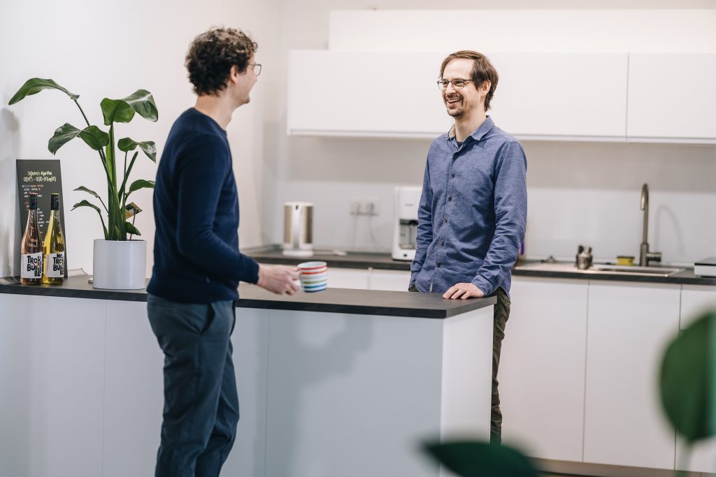 Zwei Männer stehen lächelnd in der Küche und unterhalten sich.